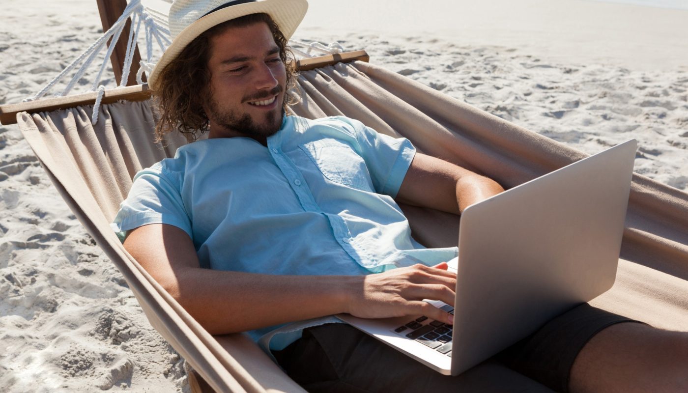 Man relaxing on hammock and using laptop on the beach