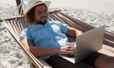 Man relaxing on hammock and using laptop on the beach