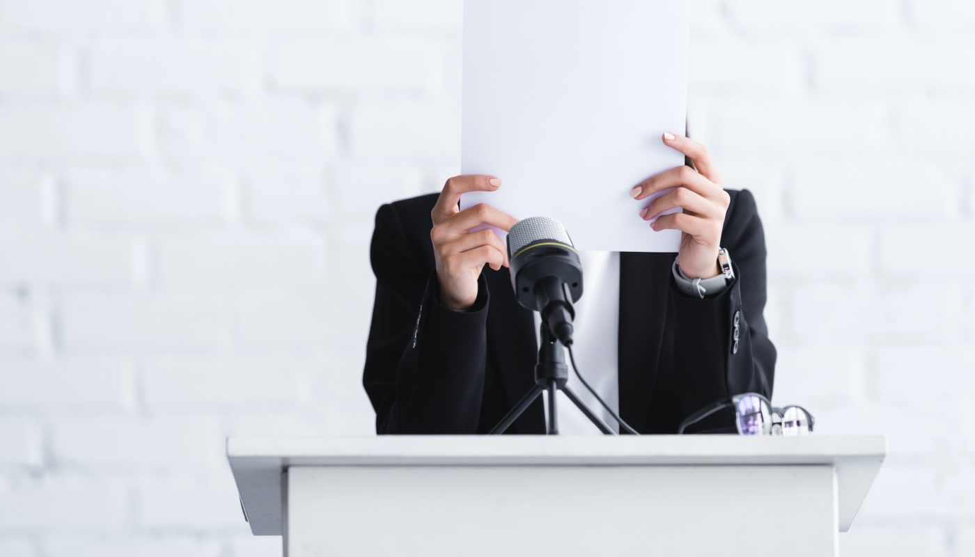 young lecturer, suffering from fear of public speaking, standing on podium tribune and hiding face